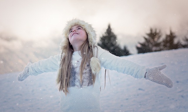 a girl in a fur hat and mittens looking up into the snow